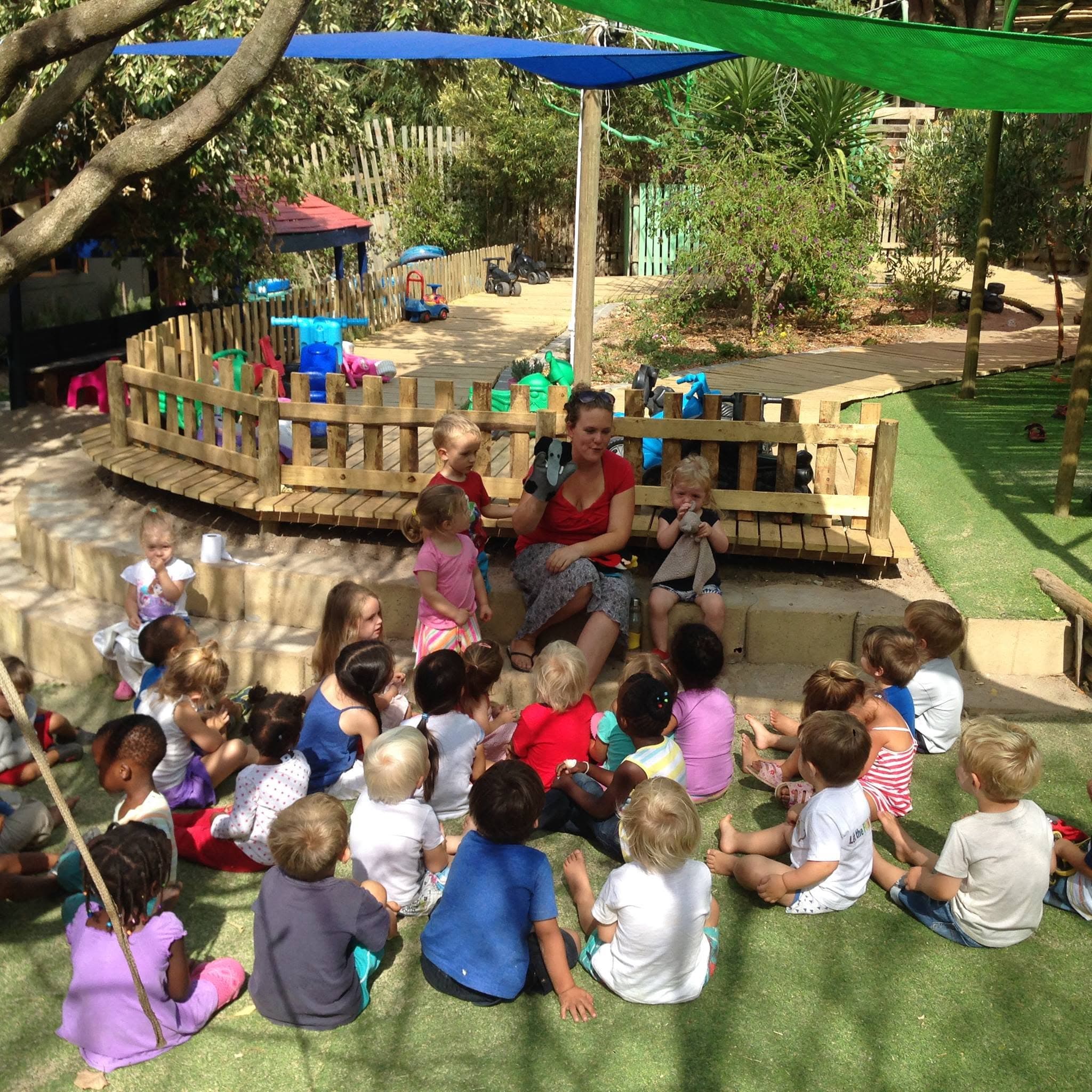 An educator reading a story to a big group of children in the garden