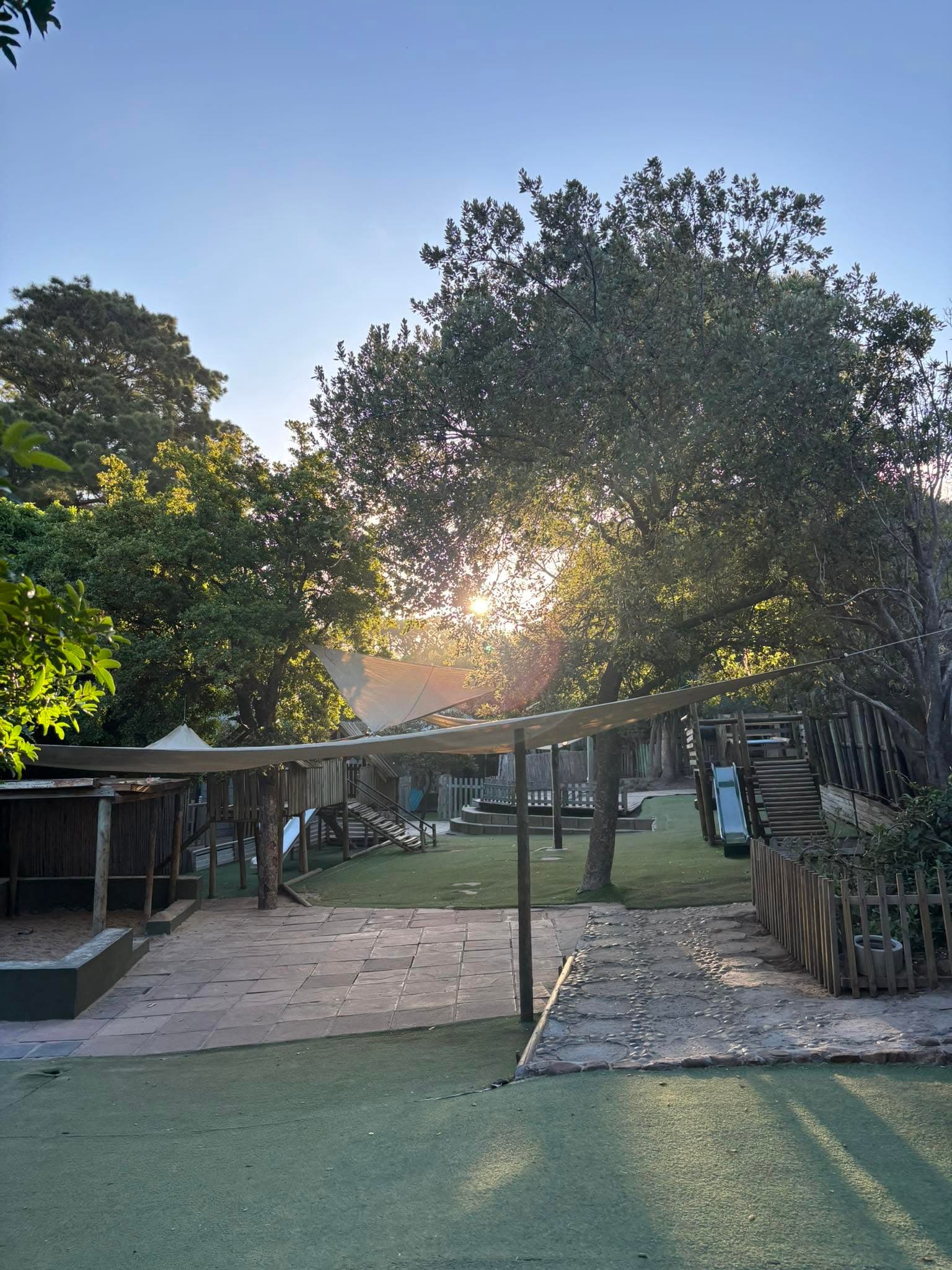 The play garden at golden hour, with slides and shade sails among the trees