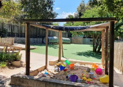 The shaded sandpit play area filled with buckets and toys